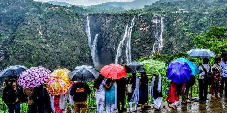 A group of people holding umbrellas standing in front of a majestic waterfall.